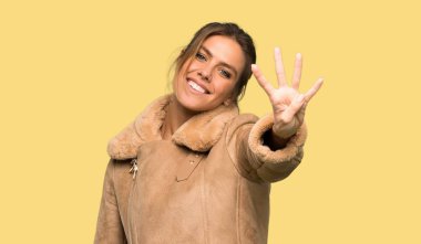 Bir ceket mutlu sarışın kadın ve izole sarı arka plan üzerinde parmakları ile dört sayma