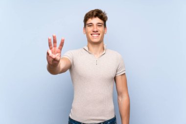Izole mavi duvar üzerinde Yakışıklı genç adam mutlu ve parmakları ile üç sayma