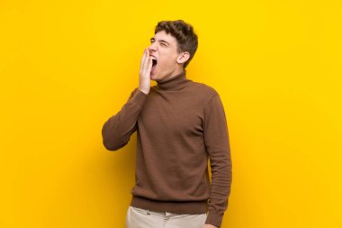 Izole sarı arka plan esneme üzerinde Yakışıklı genç adam esneme ve el ile geniş açık ağız kapsayan