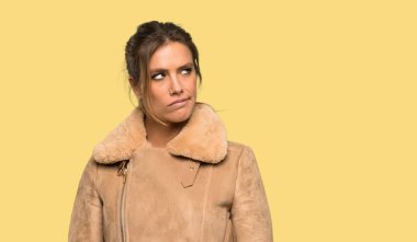 Izole sarı arka plan üzerinde dudak ısırır ise yüz ifadesi karıştırılmış bir ceket ile Sarışın kadın