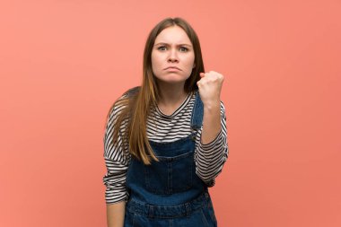 Kızgın jest ile pembe duvar üzerinde tulum ile genç kadın