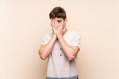 Gözleri kaplayan ve parmaklardan bakan izole arka plan üzerinde Yakışıklı genç adam