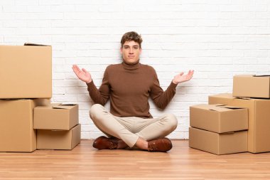 Yakışıklı genç adam kutuları arasında yeni bir evde hareketli yüz ifadesi karıştırarak şüpheleri olan