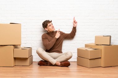 Yakışıklı genç adam işaret parmağı ile işaret kutuları arasında yeni bir evde hareket harika bir fikir