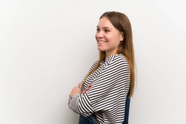 Beyaz duvar üzerinde dungarees genç kadın ayakta ve yan bakıyor