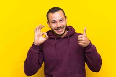 Sarı duvar üzerinde kazak ile Kolombiyalı adam ok işareti ve başparmak kadar jest gösteren