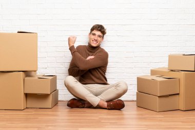 Yakışıklı genç adam güçlü jest yapma kutuları arasında yeni bir evde hareket