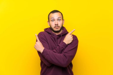 Sarı duvar üzerinde sweatshirt ile Kolombiyalı adam şüpheleri olan laterals işaret