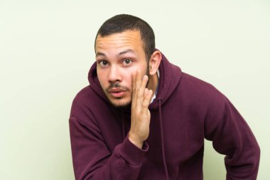 Yeşil duvar üzerinde sweatshirt ile Kolombiyalı adam bir şey fısıldıyor