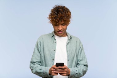 Izole mavi duvar üzerinde genç afro-Amerikan adam cep ile bir mesaj göndererek