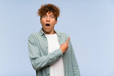 Izole mavi duvar üzerinde genç afro-amerikan adam şaşırttı ve tarafı işaret