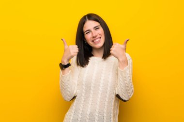 Jest kadar başparmak ve gülümseyerek izole sarı duvar üzerinde genç kadın