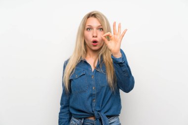 Izole beyaz duvar üzerinde genç sarışın kadın şaşırttı ve ok işareti gösteren