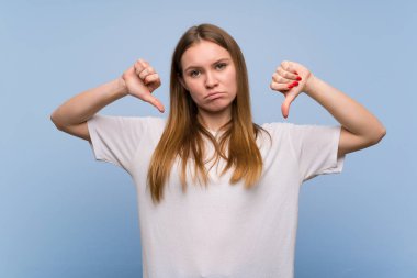 Mavi duvarın üzerinde iki eliyle başparmak aşağı gösteren genç kadın