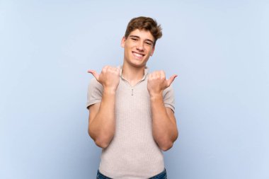 Jest kadar başparmak ve gülümseyerek izole mavi duvar üzerinde Yakışıklı genç adam