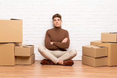 Yakışıklı genç adam kollarını çapraz tutan kutular arasında yeni evde hareket