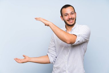 Bir reklam eklemek için copyspace tutan izole mavi duvar üzerinde Kolombiyalı adam
