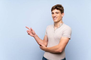 Izole mavi duvar üzerinde yakışıklı genç adam yan parmak işaret