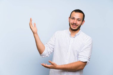 Izole mavi duvar üzerinde Kolombiyalı adam gelmeye davet için yan ellerini uzatan