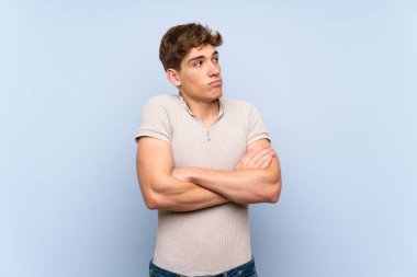 Izole mavi duvar üzerinde yakışıklı genç adam omuzları kaldırırken şüphe jest yapma