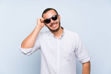Gözlük ve gülümseyen izole mavi duvar üzerinde Kolombiyalı adam