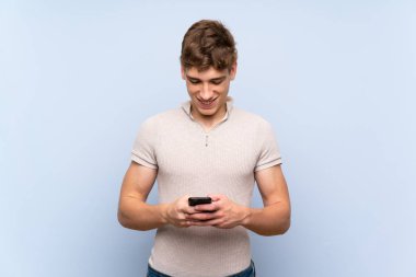 Cep telefonu ile bir mesaj göndererek izole mavi duvar üzerinde Yakışıklı genç adam