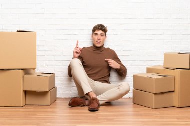 Yakışıklı genç adam sürpriz yüz ifadesi ile kutular arasında yeni evde hareket