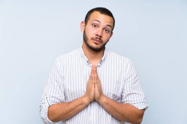 İzole mavi duvarın üzerindeki Kolombiyalı adam avuç içini bir arada tutuyor. Kişi bir şey ister