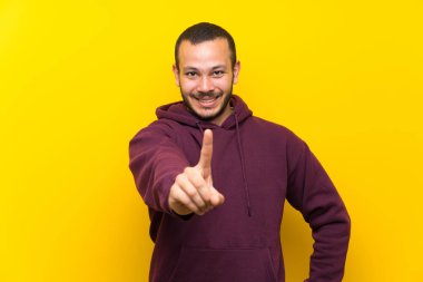 Sarı duvar üzerinde sweatshirt ile Kolombiyalı adam gösteren ve bir parmak kaldırma