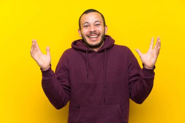Sarı duvar üzerinde Sweatshirt ile Kolombiyalı adam çok gülümseyen