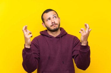 Parmaklar geçiş ve en iyi isteyen sarı duvar üzerinde Sweatshirt ile Kolombiyalı adam