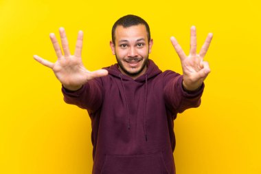 Sarı duvar üzerinde sweatshirt ile Kolombiyalı adam parmakları ile sekiz sayma