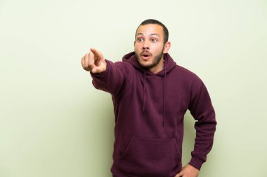 Yeşil duvar üzerinde sweatshirt ile Kolombiyalı adam uzağa işaret