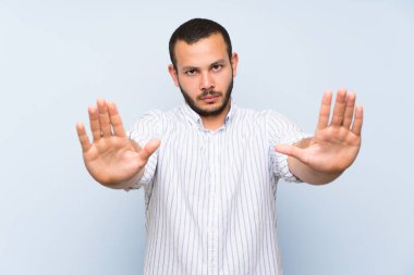 Izole mavi duvar üzerinde Kolombiyalı adam stop jest yapma ve hayal kırıklığına