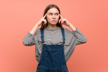 Şüpheve düşünme olan pembe duvar üzerinde tulum ile genç kadın