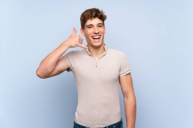 Izole mavi duvar üzerinde yakışıklı genç adam telefon jest yapma. Beni geri arayın işareti