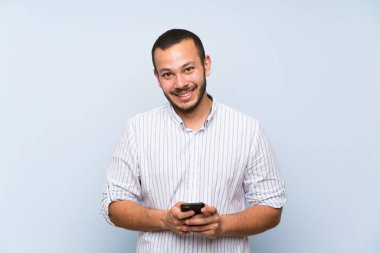 İzole mavi duvar üzerinde Kolombiyalı adam mobil bir mesaj gönderme