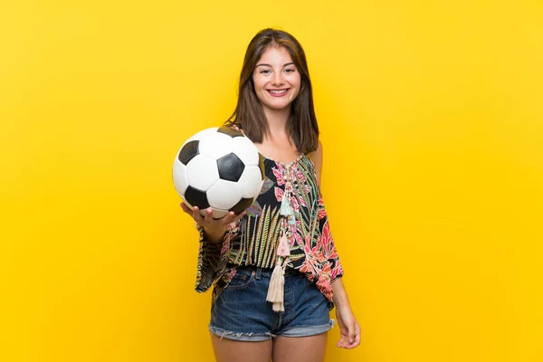 サッカーボールを保持している孤立した黄色の背景の上にカラフルなドレスを着た白人の女の子 — ストック写真