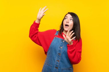 Sarı duvar üzerinde tulum ile genç Meksikalı kadın sinirli ve korkmuş