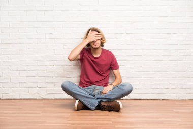 Gözleri eller tarafından kapsayan katta oturan sarışın adam. Bir şey görmek istiyor musunuz