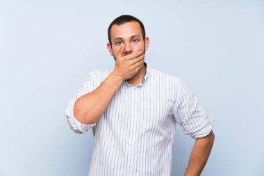 Elleri ile ağız kapsayan izole mavi duvar üzerinde Kolombiyalı adam