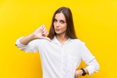 Izole sarı arka plan üzerinde genç kadın başparmak aşağı işareti gösteren