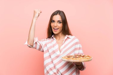 Genç kadın bir zafer kutluyor izole pembe duvar üzerinde bir pizza tutan