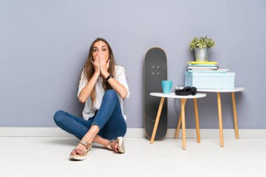 Genç bir kadın yerde oturuyor ve yüzünde sürpriz bir ifade var.