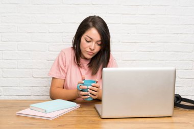 Elinde bir fincan kahve tutan dizüstü bilgisayarı olan meksikalı genç kadın