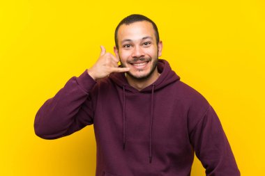 Sarı duvar üzerinde kazak ile Kolombiyalı adam telefon jest yapıyor. Beni geri arayın işareti
