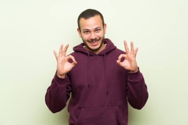 Parmakları ile ok işareti gösteren yeşil duvar üzerinde sweatshirt ile Kolombiyalı adam