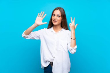İzole edilmiş mavi arka plan üzerinde genç bir kadın parmaklarıyla sekiz sayıyor