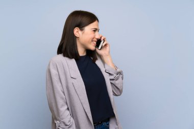 Cep telefonu ile bir konuşma tutarak izole mavi duvar üzerinde genç kadın