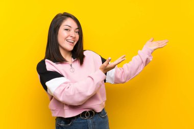 Izole sarı arka plan üzerinde genç Meksikalı kadın gelmeye davet için yan ellerini uzatarak
